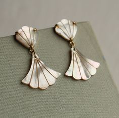 These beautiful Art Deco style mermaid earrings are pure Mother of Pearl which has been carved into a simple scalloped fan shape.  The pearl has an incredible sheen and take on a subtle glow when they catch the light.  The earring posts are made from gold plated brass.   The length of the earrings is just under 50mm (two inches), with the earring designed to hang around the jawline.   🖤 FASTER SHIPPING 🖤 Need this fast? We offer a Faster Shipping option here: https://www.etsy.com/uk/listing/100107311/faster-shipping-priority-post-upgrade 🖤 GIFT MESSAGE & WRAP SERVICE! 🖤 https://www.etsy.com/uk/listing/750160511/gift-wrap-wrapping-personalised-card?ref=listings_manager_table Pearl Mermaid, Manager Table, Wedding Day Gifts, Mermaid Earrings, Earrings Art, Earrings Bridesmaid, Modern Bridal, Bridesmaid Bracelet, Earring Posts