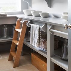 a kitchen counter with bowls on it next to a wooden step ladder and baskets in front of the sink