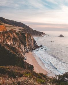 an ocean view with waves crashing on the shore and cliffs in the background at sunset