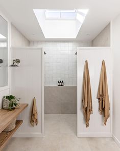 a white bathroom with two brown towels hanging on the wall and a skylight in the ceiling