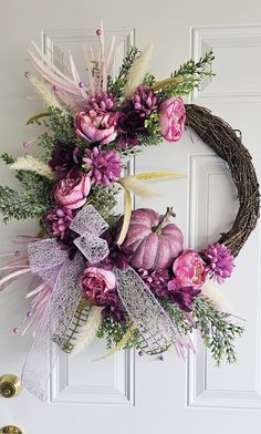 a wreath with purple flowers and greenery hanging on the front door