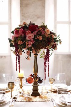 a tall vase filled with lots of flowers on top of a table next to candles