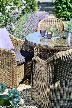 wicker patio furniture set with glass table and chairs in garden setting, surrounded by flowers