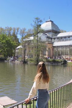 a woman standing on the edge of a railing looking at a body of water with pavilions in the background