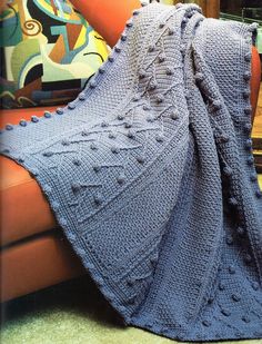 a blue blanket sitting on top of a couch next to a brown chair and pillow