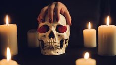 a human skull with red eyes surrounded by candles