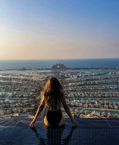 a woman sitting on the edge of a swimming pool looking out over a city and ocean