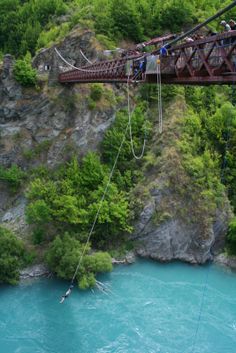 people on a bridge over a river with blue water and green trees in the background