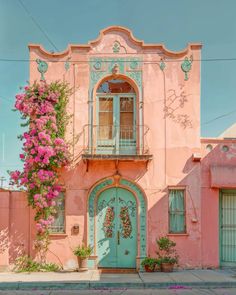 an old pink building with blue doors and flowers on the outside, against a blue sky