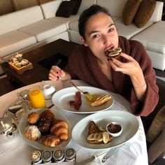 a woman sitting at a table with plates of food in front of her and an orange juice