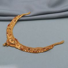 an elaborate gold necklace with beads and stones on it, sitting on a blue cloth