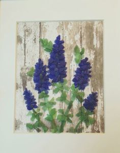 blue flowers are displayed in a white frame on a wooden surface, with green leaves