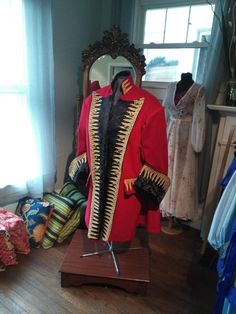 a mannequin wearing a red coat and gold trimmings stands in front of a mirror