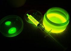 a green light in the dark next to a syringe and some plastic containers