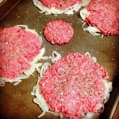 four hamburger patties cooking in a pan with onions and seasoning on top, ready to be cooked