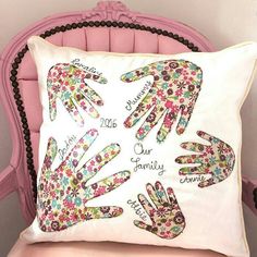 a pillow with hand prints on it sitting on a pink chair in front of a white wall