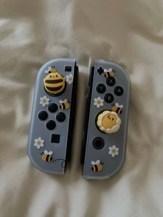 two nintendo wii game controllers sitting on top of a white bed covered in flowers and bees