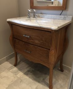 a bathroom vanity with a marble top and wooden frame around the sink, in front of a mirror