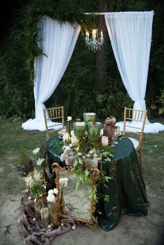 a table set up with chairs, flowers and candles for an outdoor wedding reception in the woods