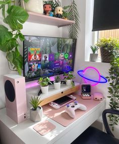 a white desk topped with a computer monitor next to a plant and a game controller