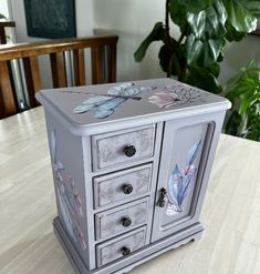 an old dresser painted with flowers and butterflies on the top, sitting on a wooden table