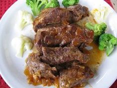 a white plate topped with meat and broccoli on top of a red table cloth