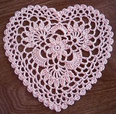 a crocheted doily in the shape of a heart on a wooden table