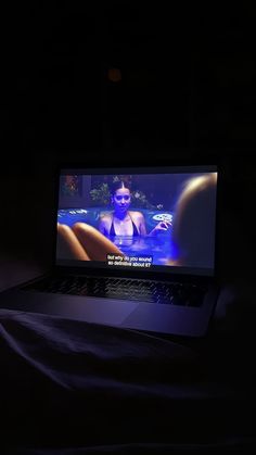 an open laptop computer sitting on top of a bed in the dark with someone's image on screen