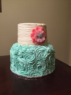 a three tiered cake with blue icing and a pink flower on top