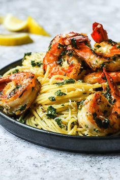 pasta with shrimp and spinach in a black bowl on a marble countertop next to lemon wedges