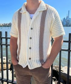 a man standing in front of the water wearing a crocheted cardigan sweater