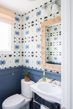 a white toilet sitting under a bathroom mirror next to a sink in a room with blue walls