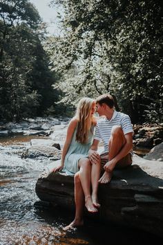 a man and woman are sitting on rocks in the middle of a river while holding each other