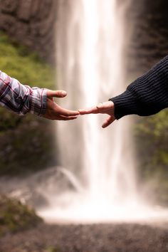 two people reaching out their hands towards a waterfall