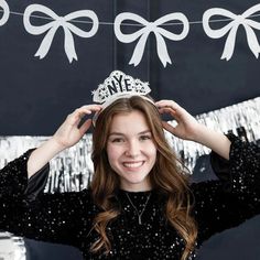 a woman wearing a tiara standing in front of a black backdrop with white bows