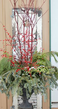 a vase filled with red berries and greenery on top of a table next to a window