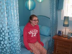 a woman sitting on top of a bed in a room with blue walls and curtains