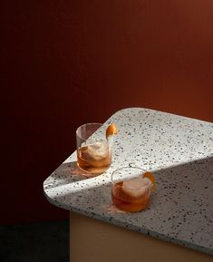 two glasses filled with liquid sitting on top of a marble counter next to a red wall