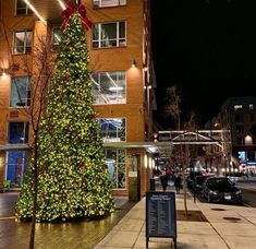 a large christmas tree is lit up in front of an apartment building on a city street