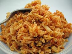 a white plate topped with rice and meat next to a silver spoon on top of a table