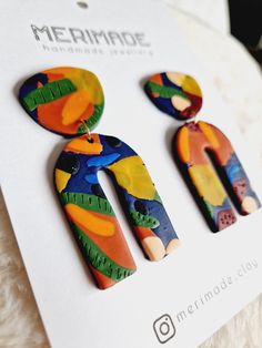 a pair of colorful earrings sitting on top of a piece of white paper next to a card