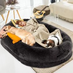 a woman laying on top of a dog bed with two dogs sleeping next to her