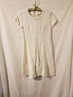 Vintage white dress with white embroidered flowers. It has a zipper down the back.  It appears to be handmade. The hem needs to be redone, most of it has come loose. There are no stains or holes. I'm not sure what the material is. It measures about 34" long, the sleeves are about 5" long at the top. The waist is about 15" across - so 30" when you double.  All items are pre-owned vintage condition. I make every effort to describe items as accurately as possible and clean them as best I can. However, sometimes something small may unintentionally get overlooked. Please feel free to ask questions or for additional photos. Read the item listing in its entirety and ask any questions before purchasing because we do not accept returns or give refunds. Thank you for visiting our shop!! Off White Floral Embroidery Short Sleeve Dress, Off White Short Sleeve Dress With Floral Embroidery, Off-white Short Sleeve Dress With Floral Embroidery, White Fitted Short Sleeve Embroidered Dress, White A-line Mini Dress With Floral Embroidery, White Fitted Knee-length Embroidered Dress, White Knee-length Embroidered Fitted Dress, White Knee-length Fitted Embroidered Dress, Vintage White Dress