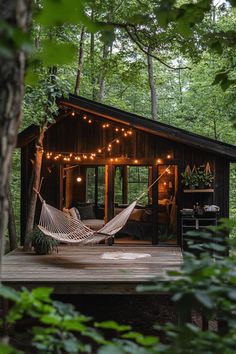 a hammock hanging from the side of a wooden cabin in the woods with string lights strung across it