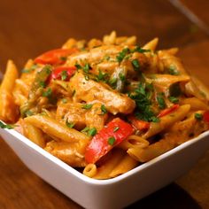 a white bowl filled with pasta covered in meat and veggies on top of a wooden table