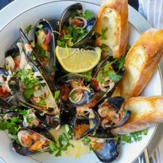 a white plate topped with mussels, bread and garnished with parsley