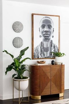 a living room with some plants and pictures on the wall above it, along with a plant potted in front of a wooden cabinet