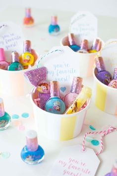 some little baskets filled with lots of different items on top of a white table and confetti