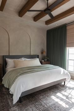 a bedroom with a bed, ceiling fan and two windows in the room that have green drapes on them