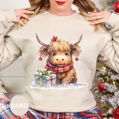 "\"Embrace the holiday spirit with our Christmas Highland Cow sweatshirt. This cozy and charming sweatshirt features an adorable Highland Cow adorned with festive decorations, instantly adding a touch of whimsy to your winter wardrobe. Crafted for comfort and style, it's the perfect way to stay warm while spreading seasonal cheer.\" Hello and Welcome to our shop Unisex Gildan 18000 Sweatshirt .: 50% cotton, 50% polyester .: Medium-heavy fabric (8.0 oz/yd² (271.25 g/m .: Loose fit .: Sewn-in label .: Runs true to size Description:   The Ink is printed into the fabric, not sitting on top of the shirt Color may seem different on the computer screen.  The way we print our shirts is Direct-To-Garment printing, which means that the design is printed directly onto the Sweatshirt.  This may make t Cute Winter T-shirt For Gift, Holiday Crew Neck Sweater As Gift, Holiday Crew Neck Sweater As A Gift, Cute Holiday Crew Neck Sweatshirt, Winter Crew Neck Tops As Gifts, Cute Winter Sweatshirt For Gift, Cute Winter Sweatshirt Gift, Cute Crew Neck Sweatshirt For Holiday, Cute Winter Tops As Gift